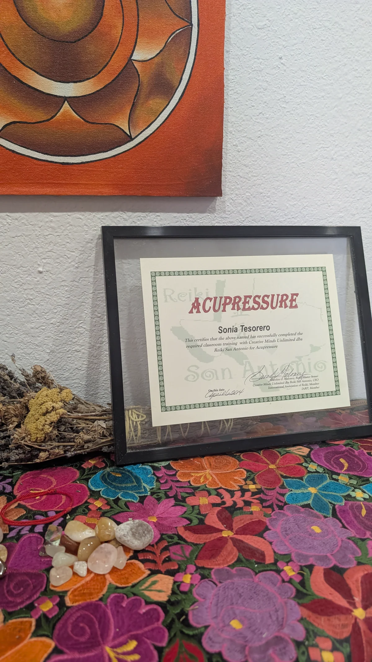 Sonia’s framed acupressure training certificate beside embroidered cloth and stones