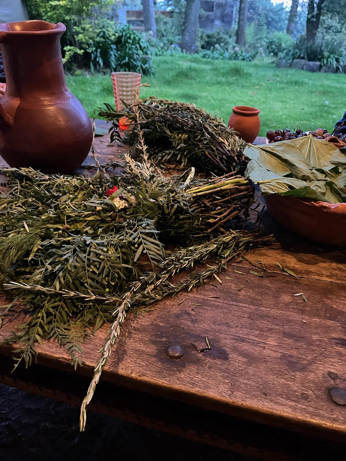 A wider view of herbs, fruit and clay vessels on a table in Mexico.