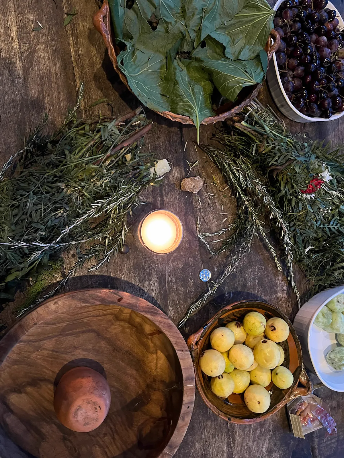 An overhead view of herbs, fruit, a candle and vessels on a wooden table in Mexico.
